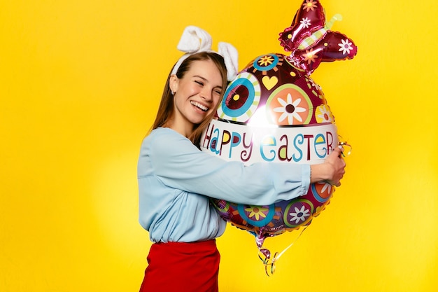 Charming woman wearing bunny ears, hugging egg shape balloon