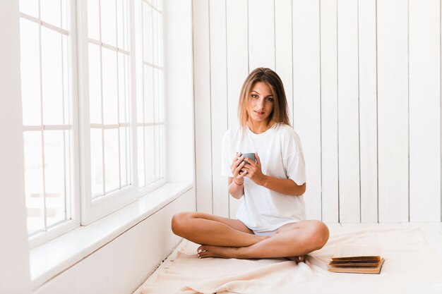 Charming woman with beverage sitting near window