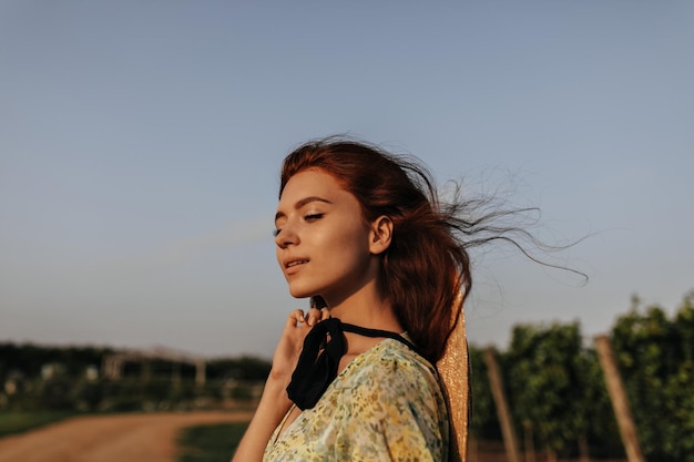 Charming woman with ginger hairstyle cute freckles and dark bandage on neck in green and yellow modern clothes posing outdoor