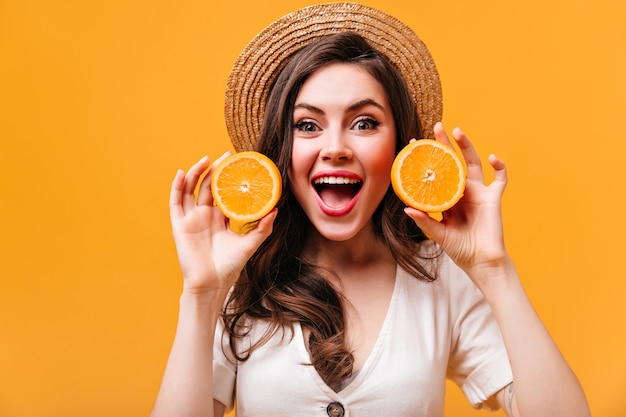 Charming woman with green eyes looks into camera with delight and holds oranges on isolated background