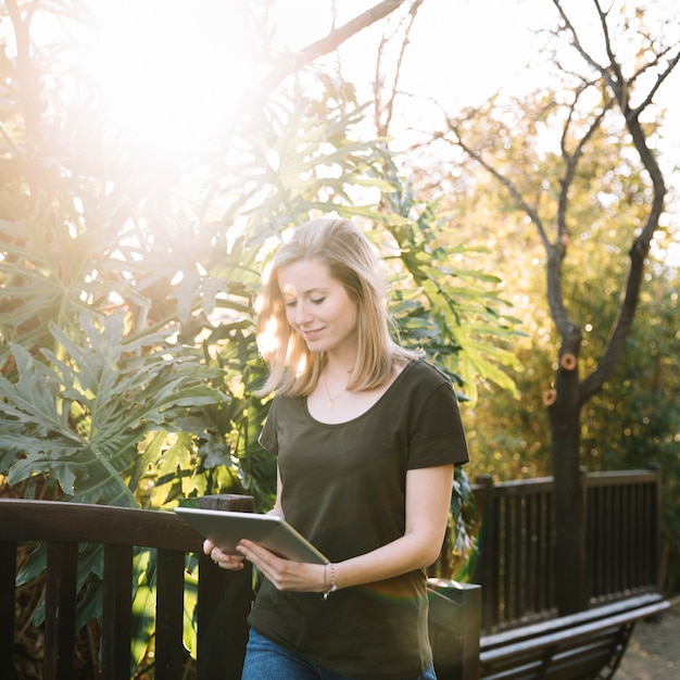 Charming woman with tablet walking in park