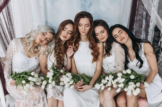 Free photo charming women sit side by side with bouquets of white tulips on the cosy bed