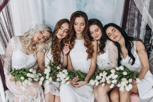 Charming women sit side by side with bouquets of white tulips on the cosy bed