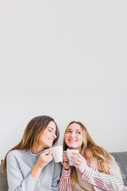 Charming women with mugs on sofa