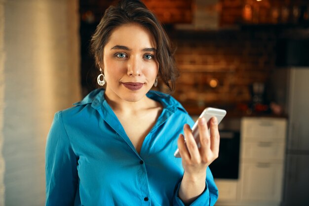 Charming young Caucasian plus size woman in blue dress holding cell phone.