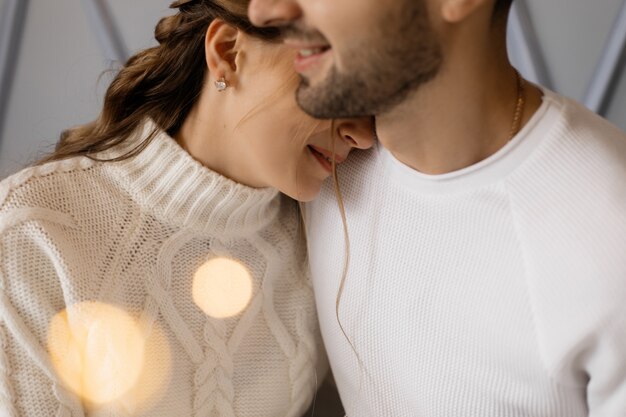 Charming young couple in cozy white home clothes poses in a room with Christmas tree