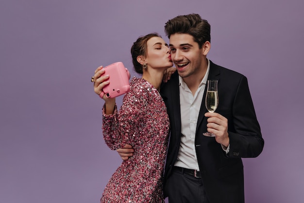カメラを楽しんだり、写真を作ったり、ワインを飲んだり、薄紫色の壁に素敵なポーズをとってパーティー服を着た魅力的な若いカップル