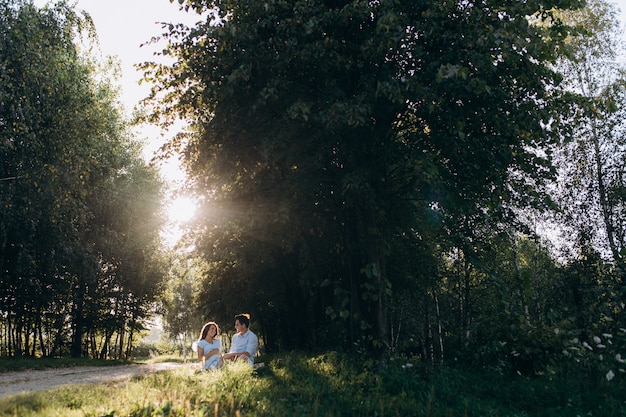 Charming young expecting couple rest on the plaid under green tree