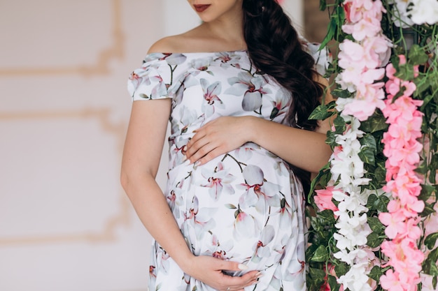 Charming young pregnant woman poses in a studio with pink flowers