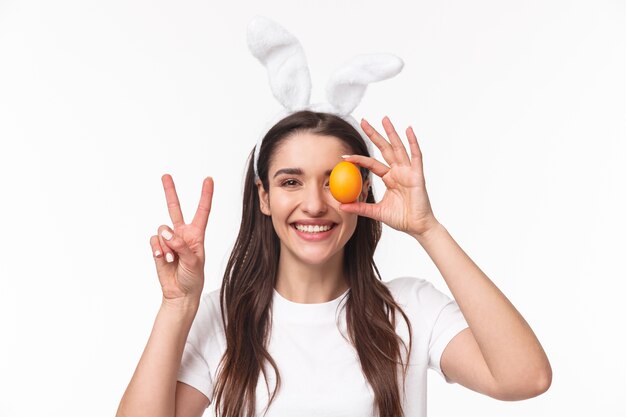 очаровательная молодая женщина в кроличьих ушах держит цветное яйцо