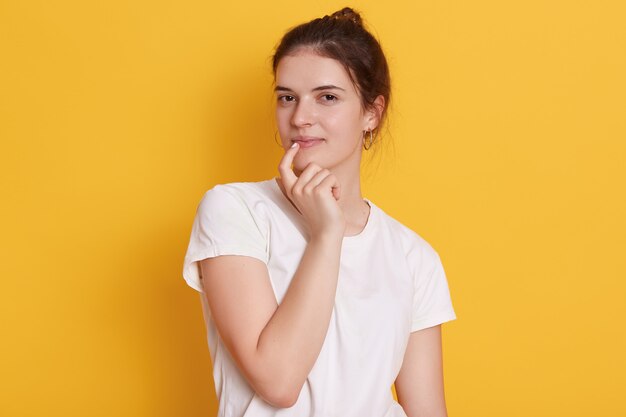 Очаровательная молодая женщина в белой футболке, держащая палец на губе