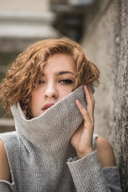 Charming young woman with short tufty hair holding raised sweater's collar