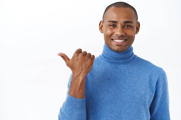 Check out my new car, its outside. Portrait of pleased, proud smiling african american male pointing thumb left and grinning satisfied