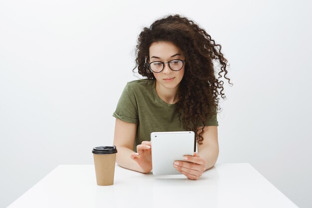 Checking schedule while waiting for client. Portrait of good-looking confident female creative coworker in glasses, sitting at table