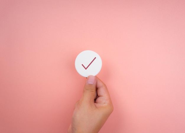 Checklist concept, minimal style. check mark icon symbols on white round sponge in hand on pink pastel background.