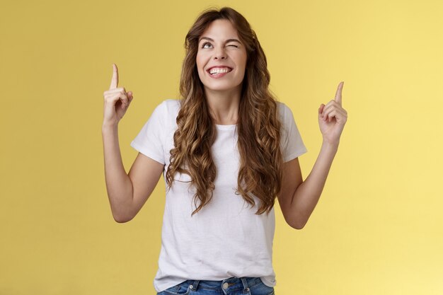 Cheeky confident positive attractive female optimistic joyful vibe smiling toothy wink grinning look up sassy pointing top making deal god hinting making cunning mood stand yellow background