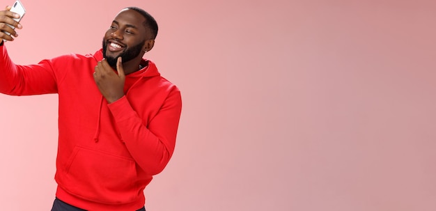 Free photo cheeky cool african american confident bearded guy in red hoodie taking selfie update date app