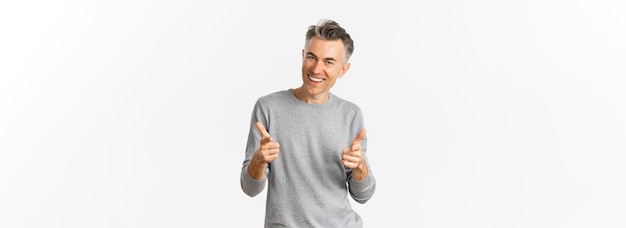 Free photo cheeky middleaged man with grey short hairstyle pointing fingers at camera and smiling praising good