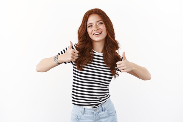 Cheeky pretty redhead girlfriend with freckles in striped t-shirt, show thumbs-up approval sign, smiling and nod acceptingly, satisfied, give positive judgement, like your choice