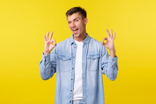 Cheeky smiling handsome man showing tongue and wink at camera, showing okay gestures totally satisfied, amazed with event, leave positive comment, recommend service or student courses.