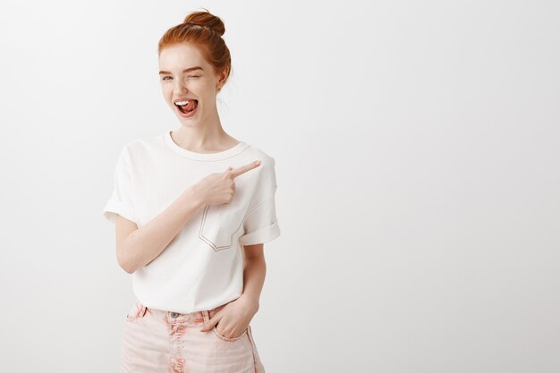 Cheeky smiling redhead girl wink and pointing finger right