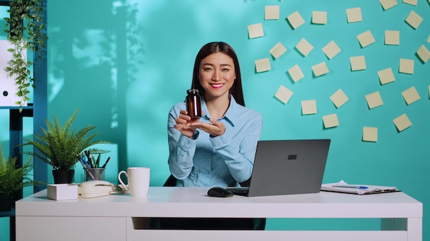 Free photo cheerful affable asian medical saleswoman proudly presenting pill bottle, showing thumbs up sign. office worker in modern relaxed colourful workplace over blue studio background