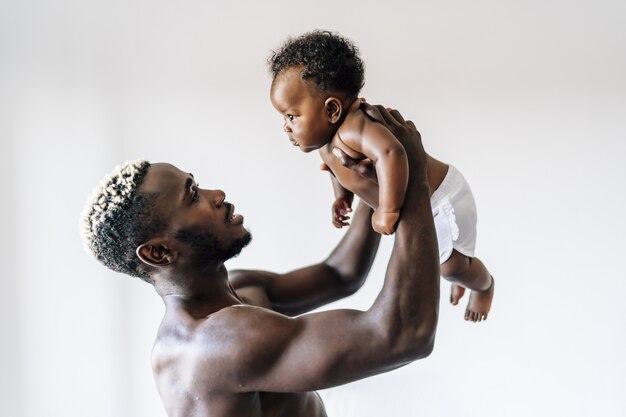 쾌활한 아프리카계 미국인 아버지가 아기를 돌보고 즐겁게 놀고 있습니다.