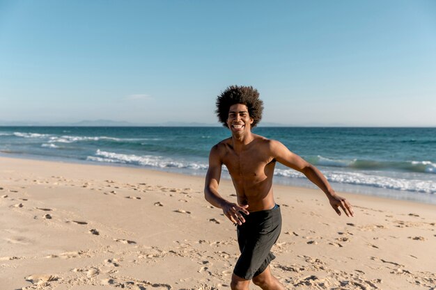 海岸で走っている陽気なアフリカ系アメリカ人男性