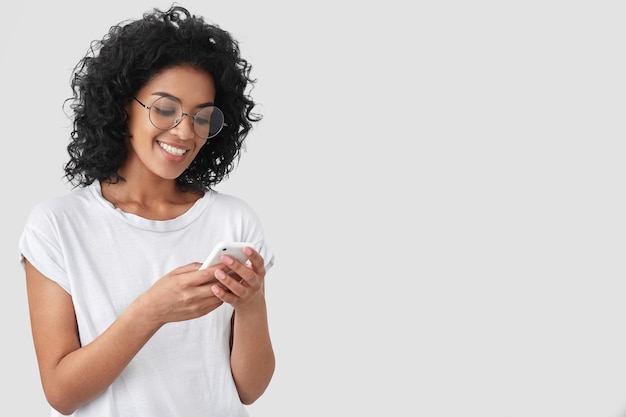 Free photo cheerful african american with crisp hair, holds modern smart phone, happy smile