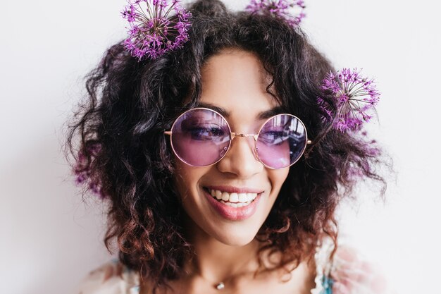 Cheerful african girl with short hairstyle posing with purple flowers. spectacular young woman in sunglasses wears alliums in hair.