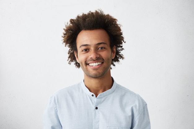 Free photo cheerful african guy with narrow dark eyes and fluffy hair dressed in elegant white shirt