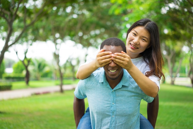 Free photo cheerful african man giving girlfriend piggyback while she covering his eyes with hands.