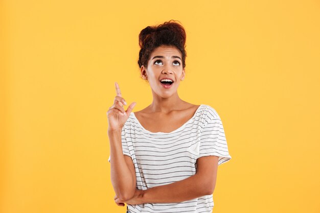 Cheerful afro-american lady pointing with finger up to copy space