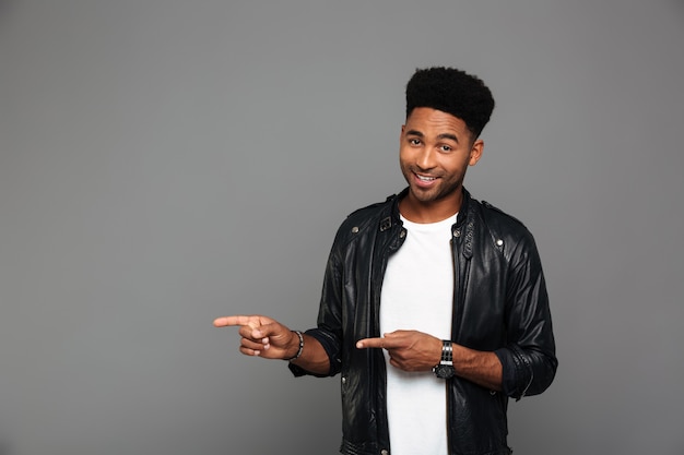 Cheerful afro american man in leather jacket pointing with two fingers, looking