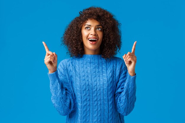 Cheerful amused african-american girl celebrating with friends new year, happy holidays, looking fireworks with excited smile, pointing looking up astonished and joyful, standing blue background.