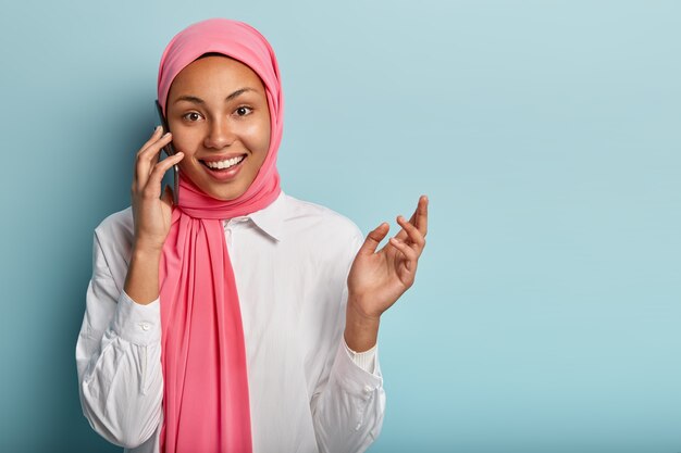 Cheerful Arabian female has telephone conversation, gestures with hands, explains something actively