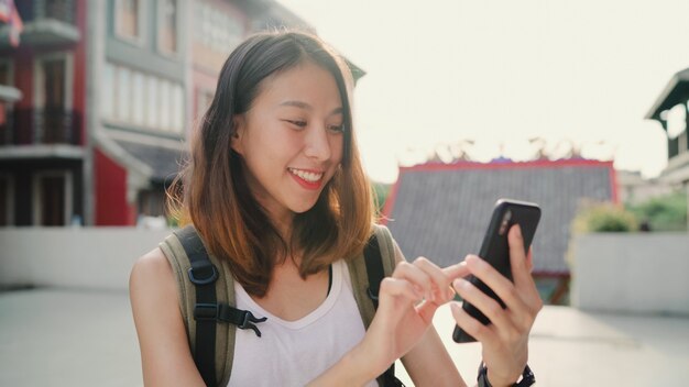 陽気なアジアのバックパッカーブロガー女性の方向と場所地図を見るのためのスマートフォンを使用して