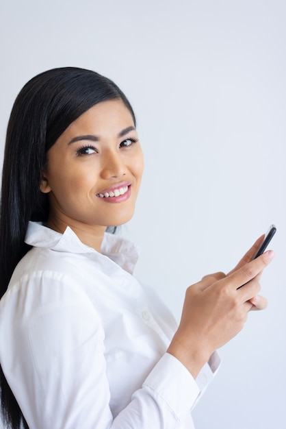 Cheerful Asian business lady with black hair using smartphone