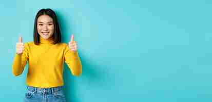 Free photo cheerful asian female model showing thumbs up gesture smiling and looking impressed praise good prod