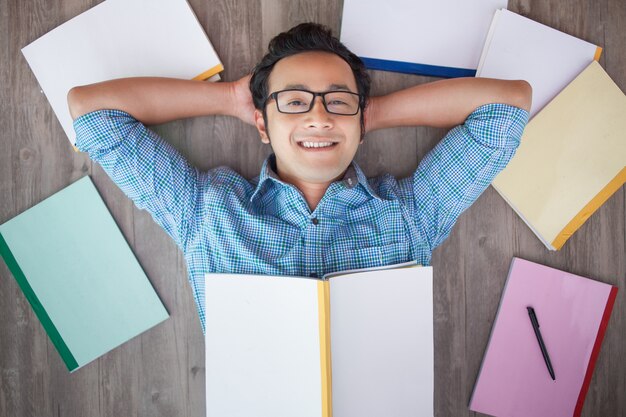 Cheerful asian guy resting on floor among books