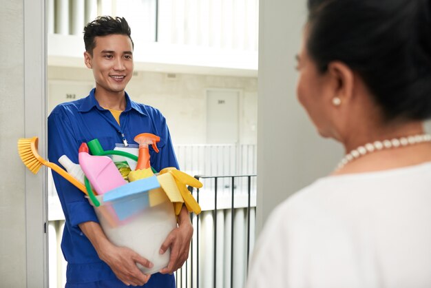 Cheerful Asian janitor with tools standing at door and talking with wealthy female homeowner