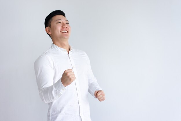 Cheerful Asian man pumping fists and looking away