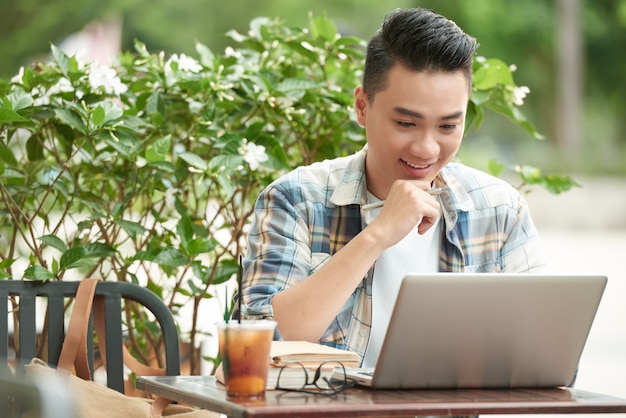 쾌활한 아시아 남자 야외 카페에 앉아 흥분과 노트북 화면을보고