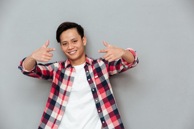 Free photo cheerful asian man standing over grey wall.