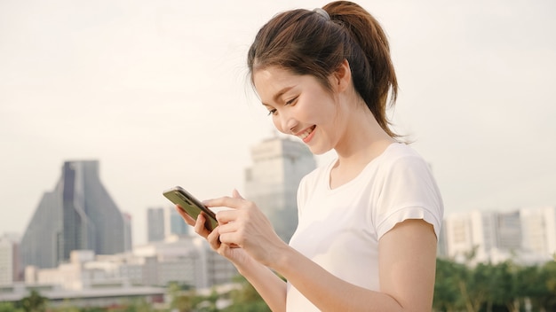 Cheerful asian tourist blogger woman using smartphone for direction and looking on location map while traveling on the street at downtown city.