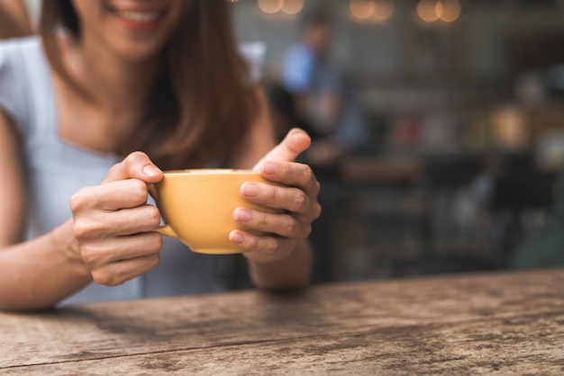 Giovane donna asiatica allegra che beve caffè o tè caldo che lo gode mentre sedendosi in caffè