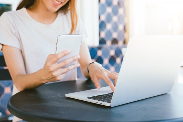 Cheerful asian young woman sitting in cafe drinking coffee and using smartphone for talking