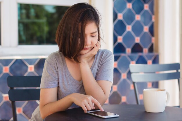 쾌활 한 아시아 젊은 여자 커피를 마시고 이야기를 위해 스마트 폰을 사용하는 카페에 앉아
