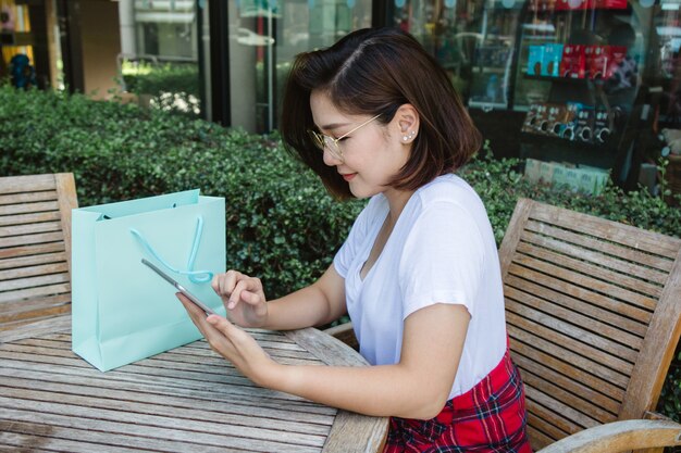 Веселая азиатская молодая женщина, сидя в кафе, используя смартфон для разговора, чтения и текстовых сообщений