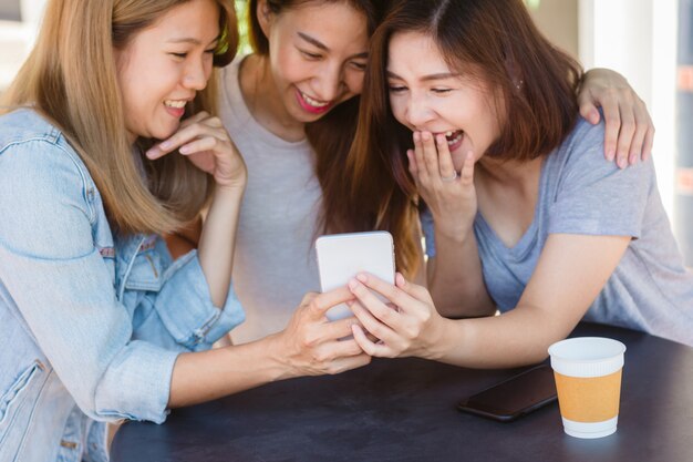 Веселые азиатские молодые женщины, сидя в кафе, пить кофе с друзьями и говорить вместе